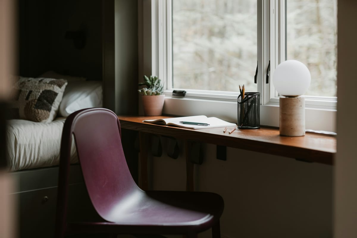 A peaceful minimalist desk setup by a window with a view of nature, featuring a warm lamp and an open notebook, symbolizing a calm inner sanctuary.