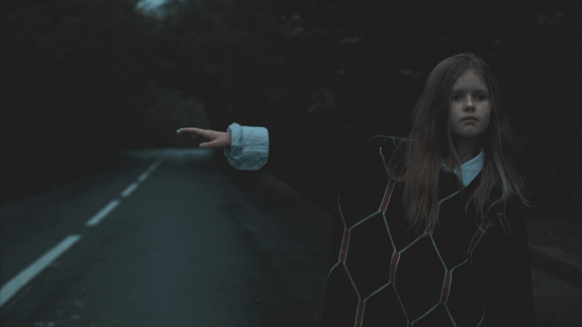 一個孤獨的小女孩在昏暗的森林馬路旁伸手攔車，象徵童年創傷與尋求生存心理救援的意象。