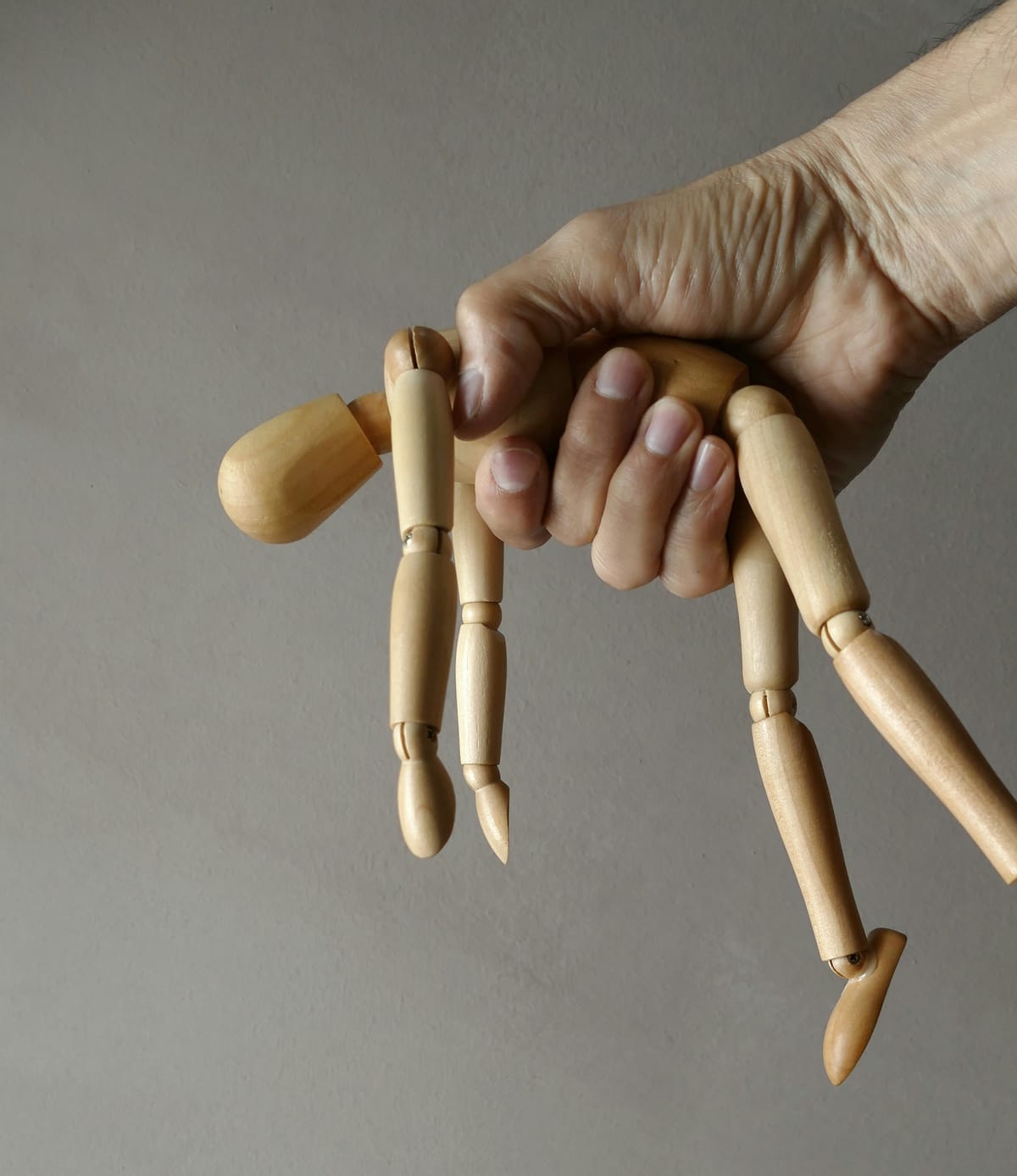 一隻手握著木製關節娃娃,象徵原生家庭中的控制與操縱,以及療癒的旅程