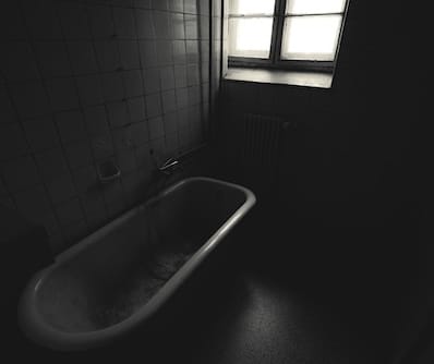 一張黑白照片，空浴缸旁是有小窗戶的牆。