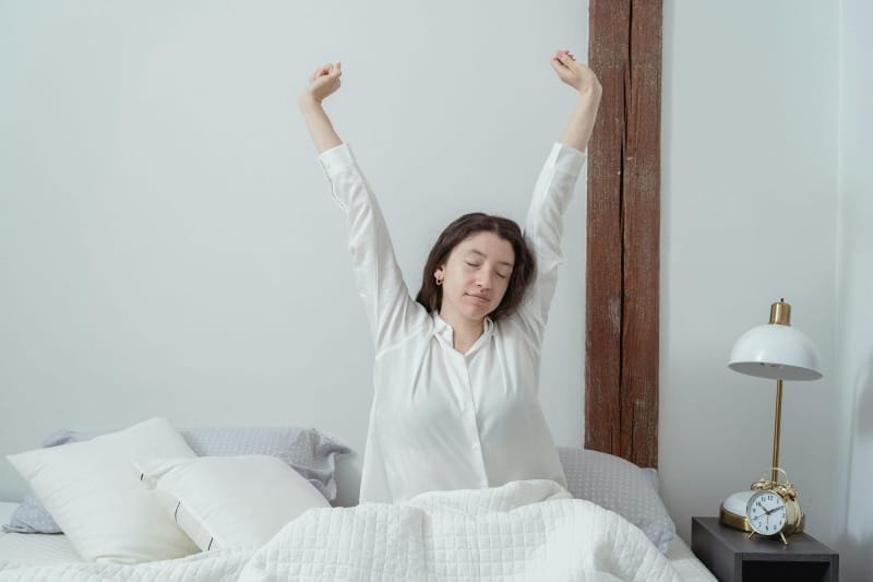 Woman stretching in bed after waking up, representing a healthy morning routine and mindful start to the day.
